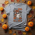 A light gray short-sleeve crewneck t-shirt featuring a Halloween-themed graphic print on the front. The graphic depicts a ghost wearing sunglasses, surrounded by pumpkins, spiderwebs, and the text 'Just a girl who loves HALLOWEN' in orange and black.